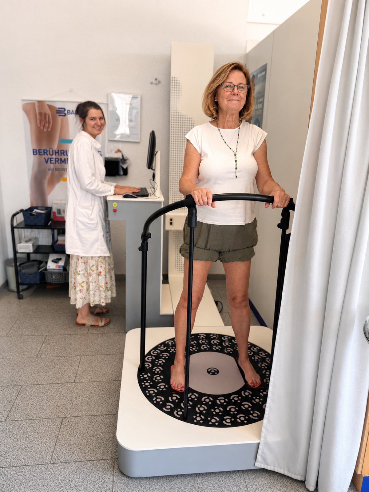 Kundin steht barfuss auf der Messplatte des Bodytronic und hält sich am Bügel fest, dahinter bedient eine Fachkraft im weissen Kittel den Rechner